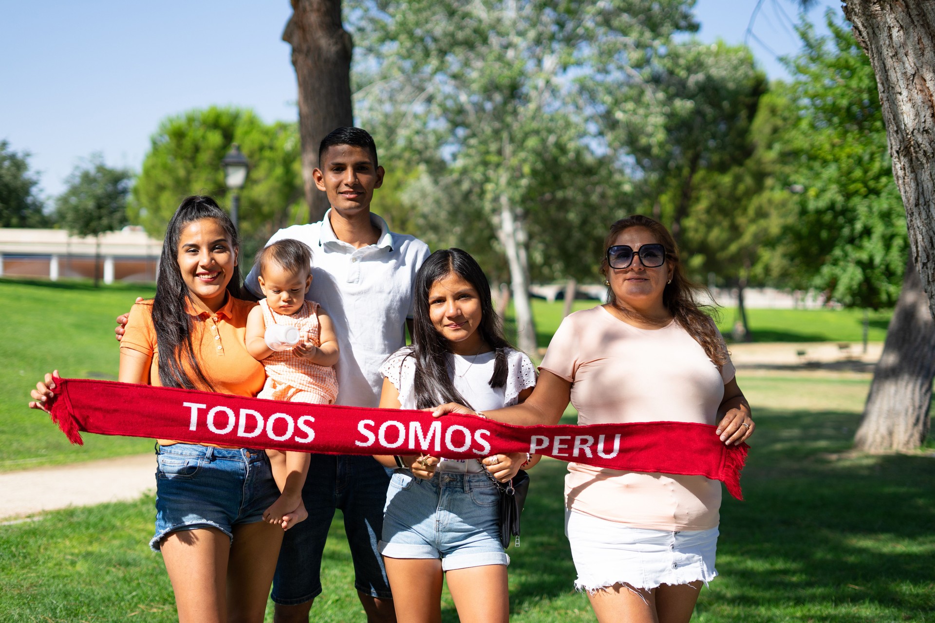 Retrato de una familia peruana multigeneracional al aire libre con un pañuelo con las palabras: Perú todos estamos en español