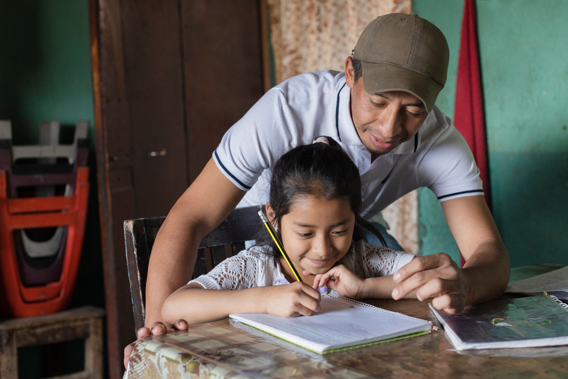 Padre hispano ayudando a su pequeña hija a hacer su tarea - Maestra enseñando a la niña a leer y escribir - Familia maya en casa