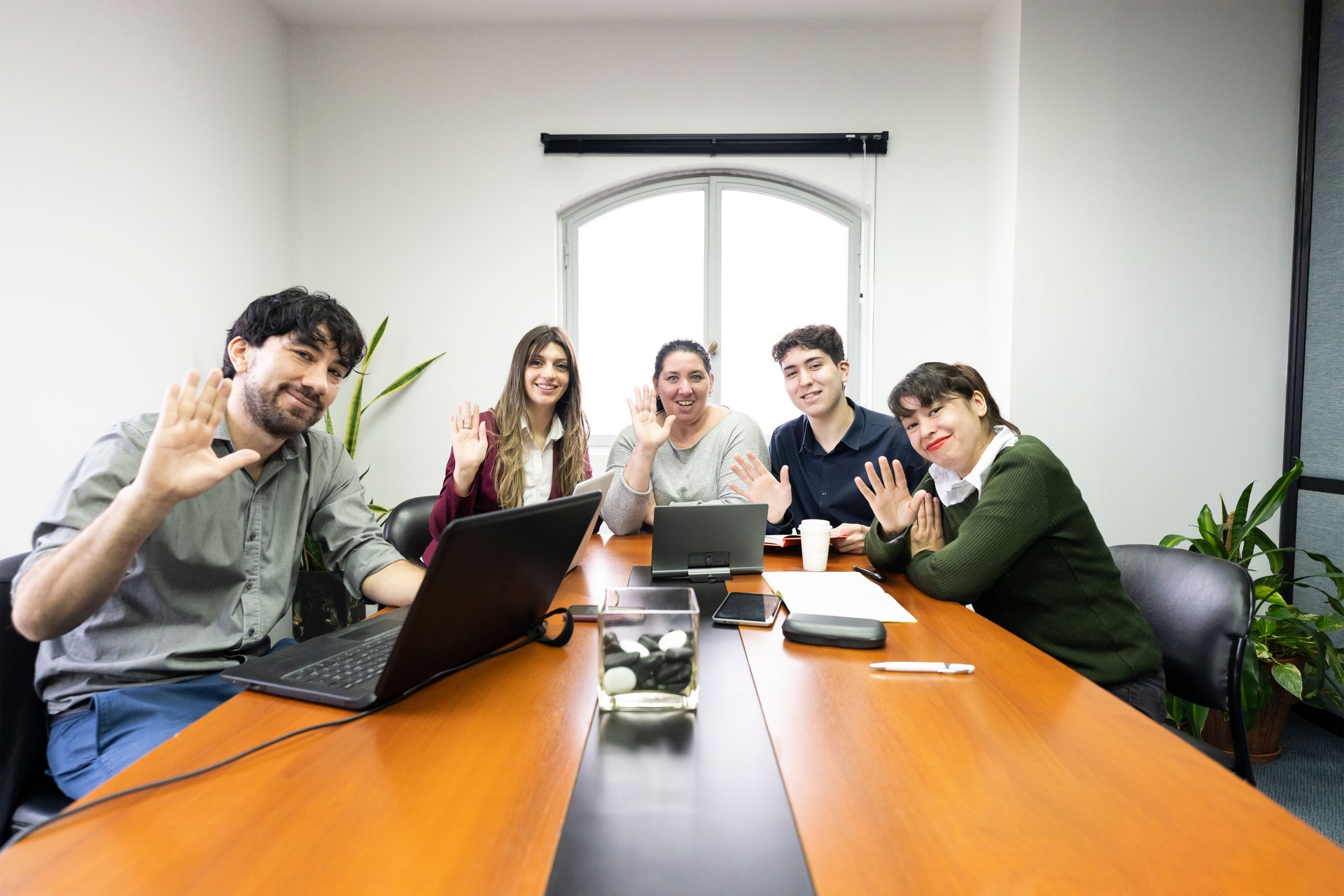 Grupo de empleados sentados en la sala de reuniones de la oficina mirando a la cámara y saludando. Concepto de reunión en línea