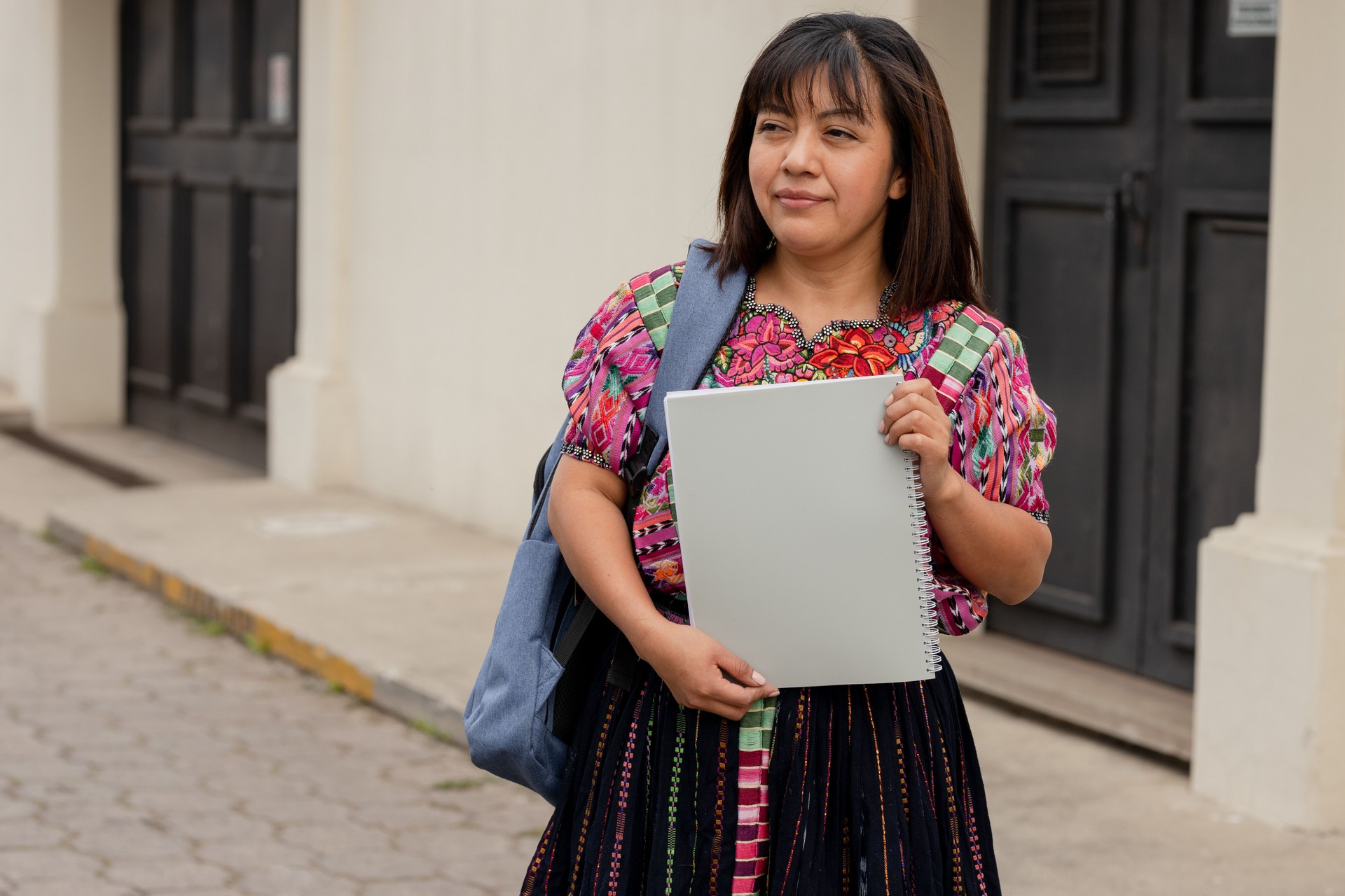 Mujer hispana con cuaderno y mochila fuera de la escuela en zona rural - Mujer maya lista para ir a estudiar - Profesora latina en la ciudad